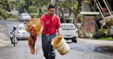 Guanacaste residents have taken to drastic measures to combat road dust in recent years.  In this photo from December 2014, a local resident carries a bucket of molasses and some material with which to spread it on the roadway.  (Photo: Adam Dietrich / La Voz de Guanacaste)